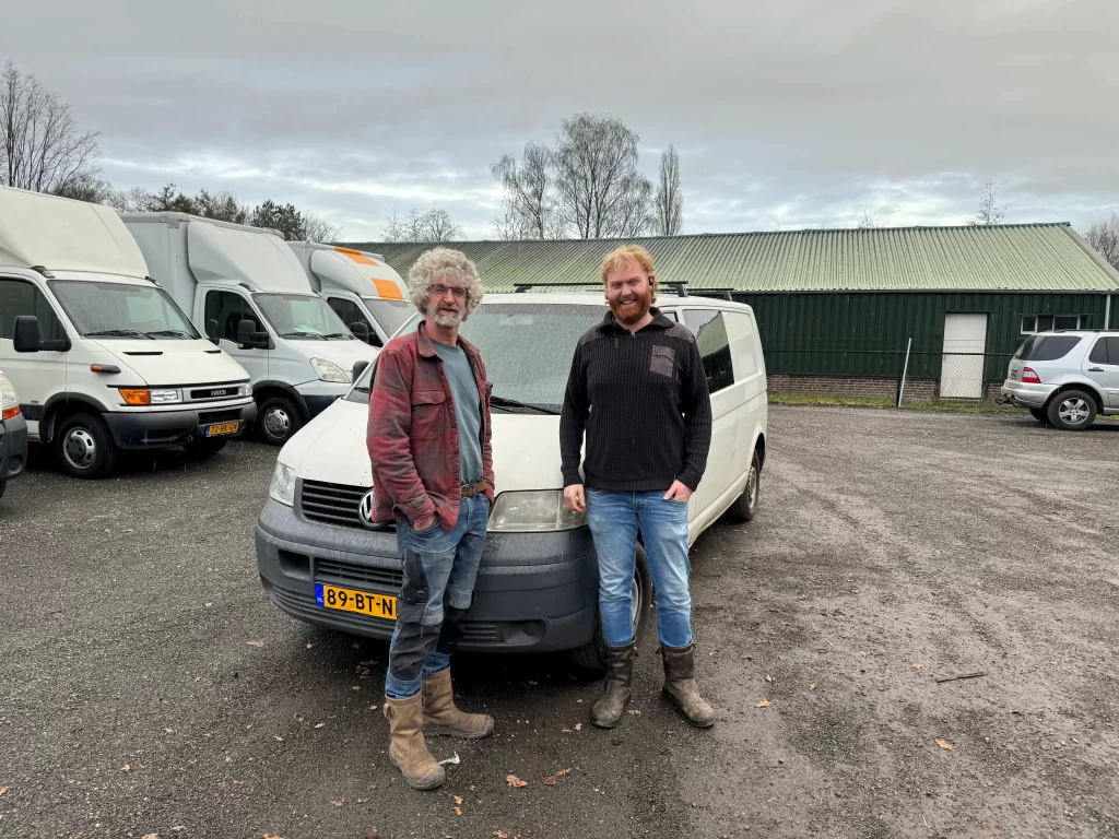 Twee mannen voor een witte Volkswagen bestelwagen op een parkeerplaats